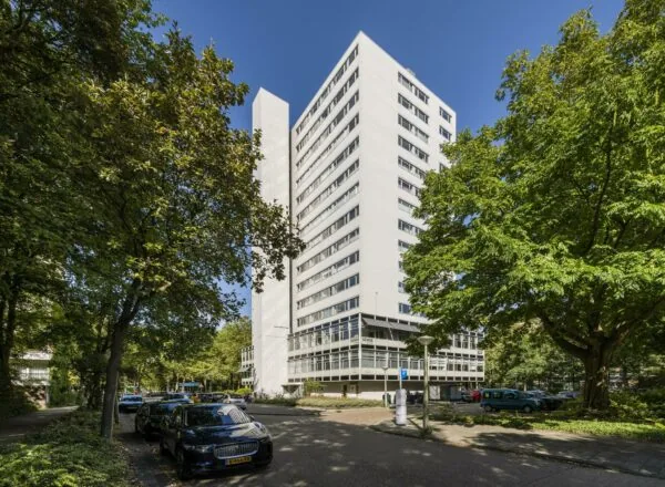 Wit hoogbouwkantoorgebouw aan de Van Leijenberghlaan, omgeven door groene bomen en geparkeerde auto's.